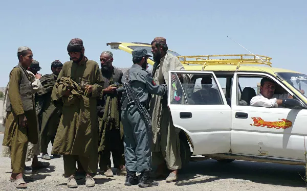 Афганский полицейский обыскивает пассажиров автомобиля, подозреваемого в перевозке наркотиков на КПП в Кандагаре